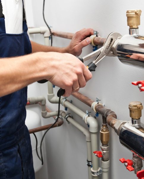 The man is installing the heater system in the house and checking pipes by the wrench