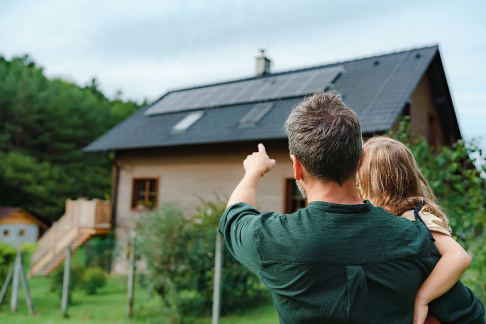 Panneaux solaires sur le toit d'une maison et présence d'un homme avec son enfant dans les bras au premier plan